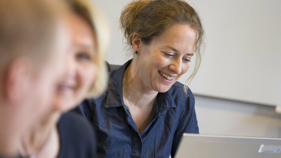 Three people in a classroom, taking a course. 